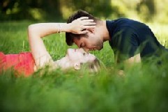 žena leží v trávě a muž ji líbá